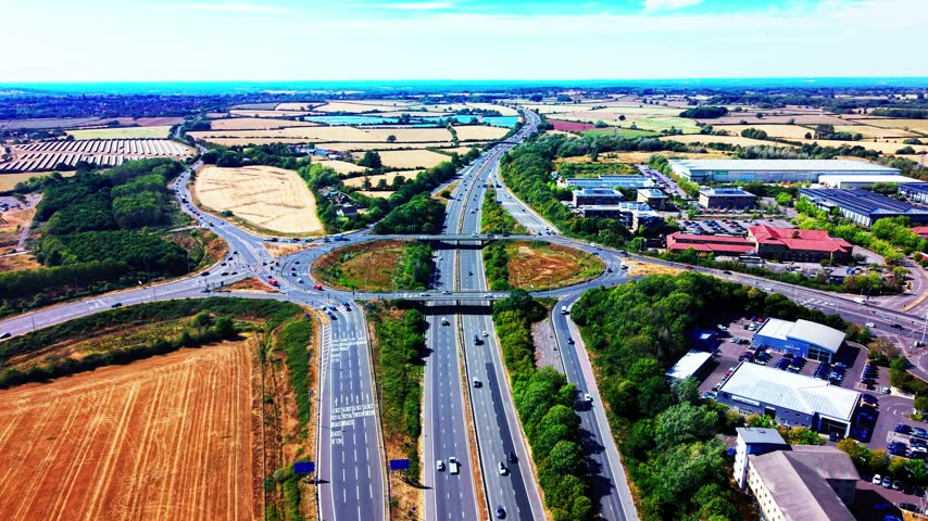Aerial view of the M4 motorway running through Wiltshire with a major road interchange, bridges, roundabouts, industrial buildings, farmland and moving traffic