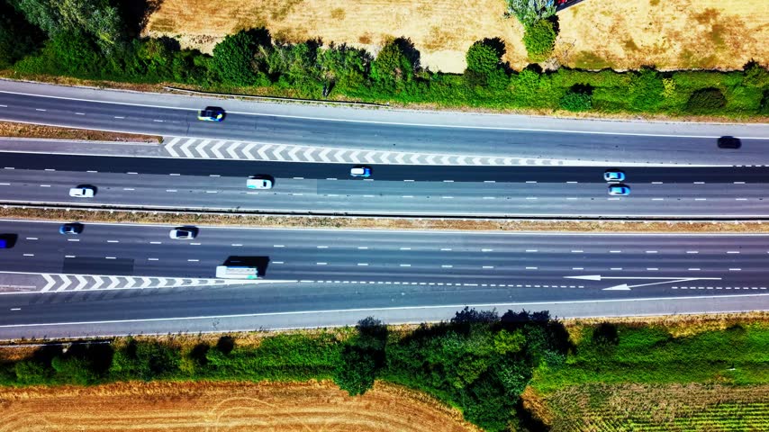 Top down aerial view of vehicles travelling along the M4 motorway in England with multiple lanes road markings slip roads and surrounding countryside
