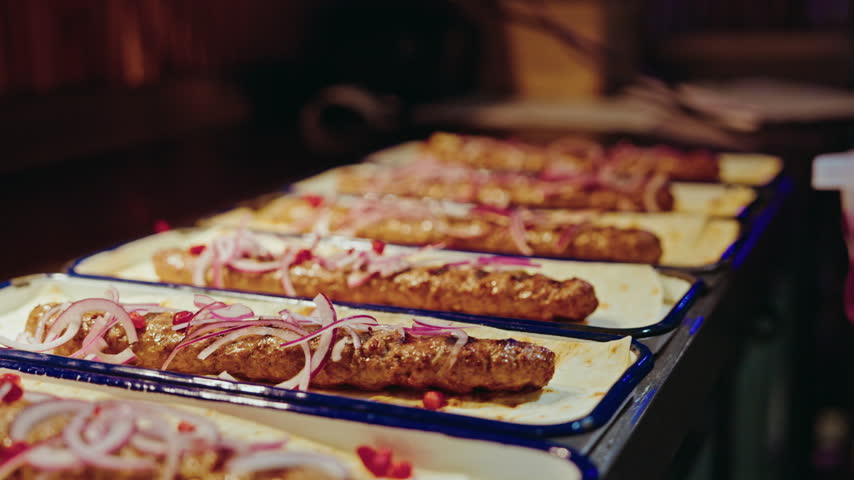 A row of plated Georgian kebabs on lavash waiting under the warm light of the restaurant pass.