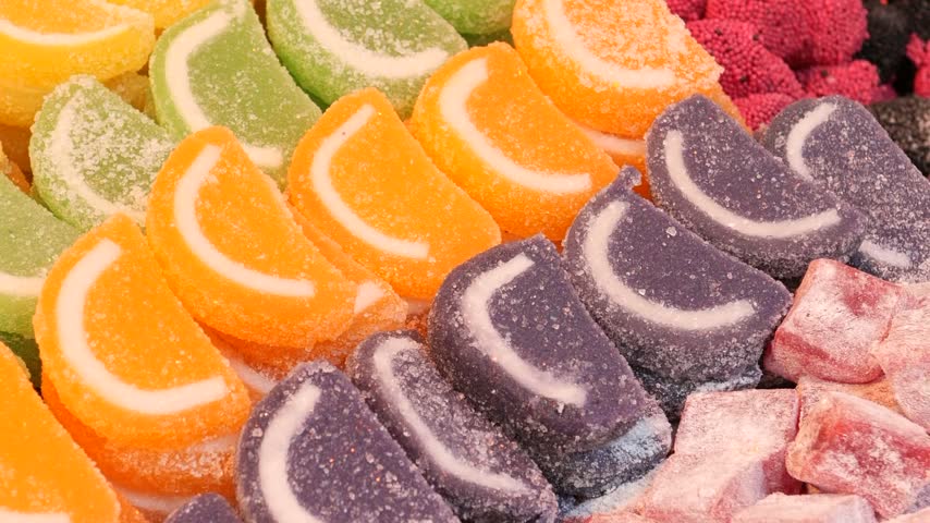 Close up overhead view of colorful sugared fruit shaped jelly candies arranged neatly in rows inside market display case. Vibrant sweet treats filmed in slow motion panning shot.