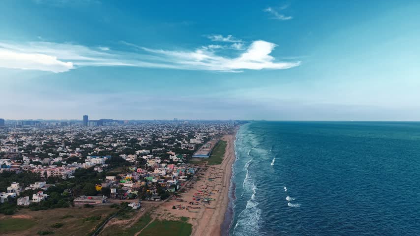 Aerial view of the expansive Marina Beach coastline with urban buildings and blue sea in Chennai, Tamil Nadu, India.
