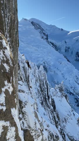Elevated panoramic view of the snow-covered Mont Blanc massif and the rocky summit of Aiguille du Midi in warm sunlight near sunset in the French Alps.