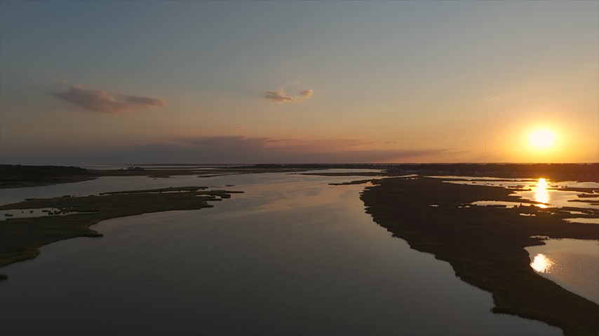 Aerial View Of Bright Sun Setting Over A Broad Tidal Channel Running Through Coastal Salt Marsh Wetlands At Sunset. Assateague National Park.