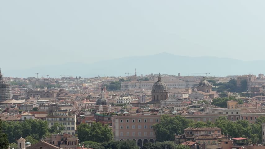 Scenic panoramic view of Rome with historic domes, terracotta rooftops and distant mountains under a clear sky.