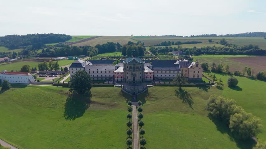 Aerial view of the historic Hospital Kuks building surrounded by lush green fields, manicured gardens, and trees in Kuks, Kralovehradecky kraj, Czechia.