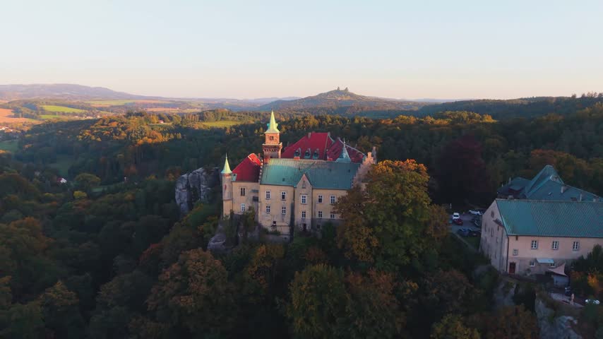 Aerial view of Zamek Hruba Skala surrounded by autumn forests and sandstone rock formations in Hruba Skala, Liberec Region, Czechia.