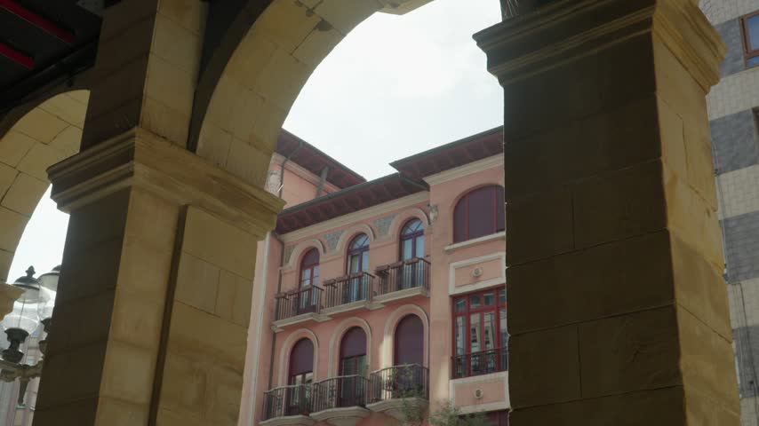 Historic building with a pink facade viewed through stone arches in Plaza Mayor of Gijon, Spain