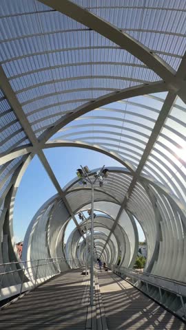 Modern architecture of the Arganzuela footbridge, also known as Perrault bridge, in the Madrid Río park with people strolling on a sunny summer day in the capital of Spain