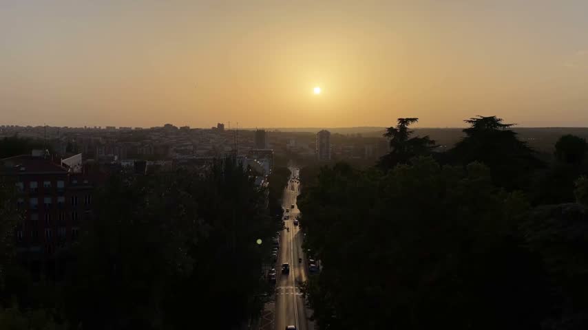 Scenic sunset over the skyline of Madrid, Spain, with the golden sun setting at the end of Calle de Segovia and casting long shadows from the trees and buildings lining the street