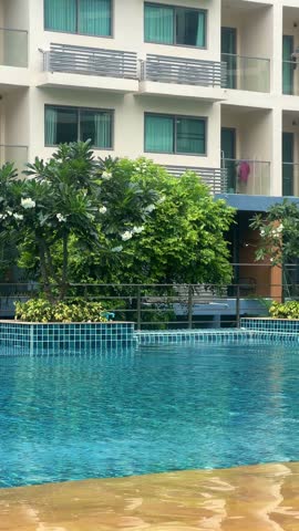 A pool with clear turquoise water at a resort in a residential complex in Pattaya, Thailand. An outdoor pool with a jacuzzi in a condominium surrounded by green trees and flowers. 4К