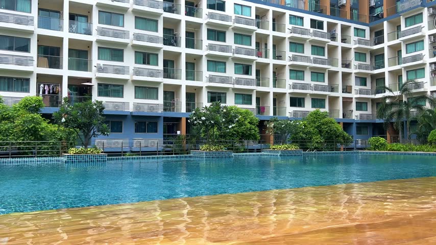 A pool with clear turquoise water at a resort in a residential complex in Pattaya, Thailand. An outdoor pool with a jacuzzi in a condominium surrounded by green trees and flowers. 4К