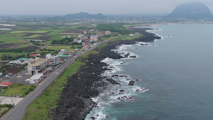 Coastal Cityscape And Road With Volcanic Rugged Coastline Near Songaksan Mountain In Seogwipo, Jeju Island, South Korea. Aerial Drone Shot