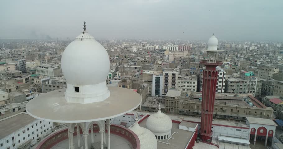 Aerial view of a mosque with white domes and a tall red minaret overlooking the dense urban landscape of old city area Karachi, Sindh, Pakistan.