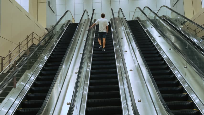 Male traveler rides upward on escalator inside modern metro station in Kuala Lumpur city, Malaysia. Public transportation, urban infrastructure, independent tourism, metropolitan mobility