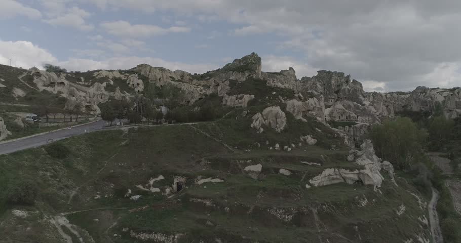 Close view of fairy chimneys with carved openings in Cappadocia, Turkey, surrounded by a rocky landscape under a cloudy sky.