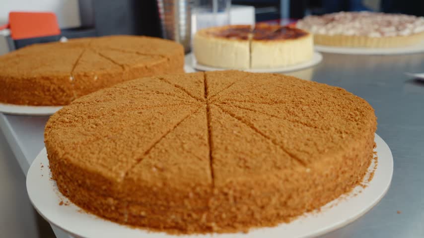 Assorted Sweet Desserts In A Pastry Shop. Various sweet desserts are arranged on cooling racks in a pastry shop. Different cakes and pastries are visible throughout the scene.