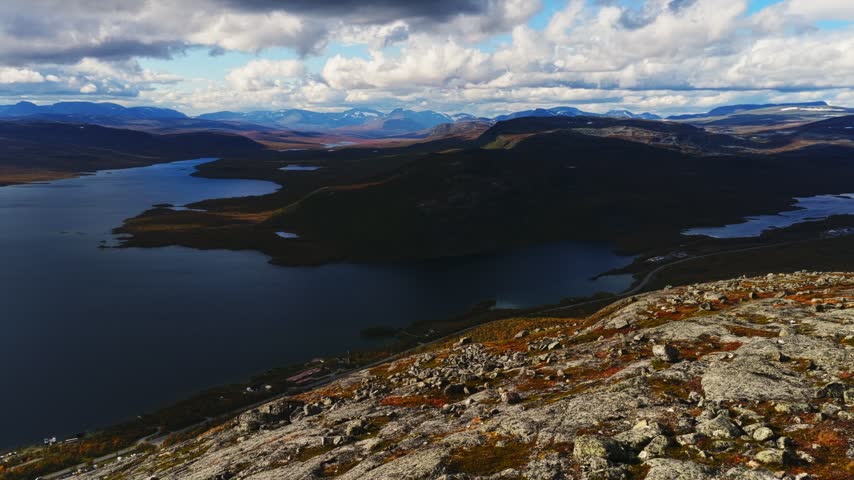 Aerial view of Kilpisjarvi lake surrounded by rocky terrain and mountains under a cloudy sky in Kilpisjarvi, Lapland, Finland.