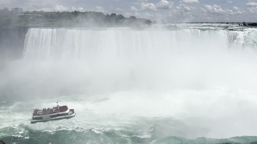 American and Horseshoe falls, Niagara Falls, Ontario, Canada. Tour boat filled with passengers navigates near the powerful Niagara Falls, surrounded by mist and rushing water