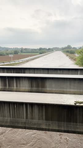 Turbulent muddy water rushes through a concrete aqueduct during a flood in Gualta, Girona, Spain