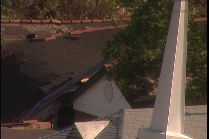 Camera zooms out from tilted church steeple to damaged and broken roofs in New Orleans after Hurricane Katrina (October 2005).