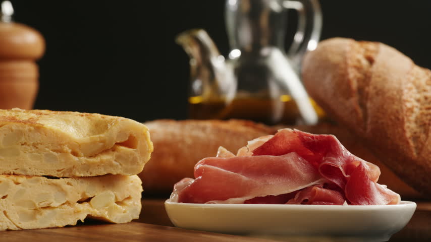 Spanish omelette with jamon serrano, tortilla and iberico cured ham appetizer on wooden table, traditional Spanish breakfast close up in cafe