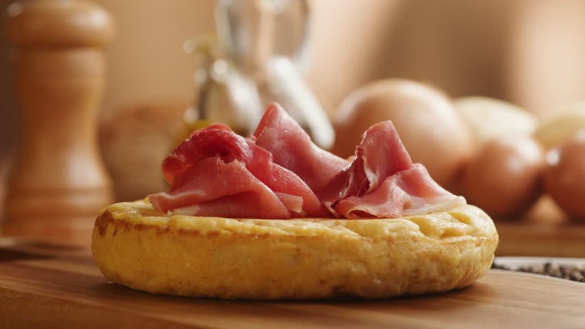 Spanish omelette with jamon serrano, tortilla and iberico cured ham appetizer on wooden table, traditional Spanish breakfast close up in cafe