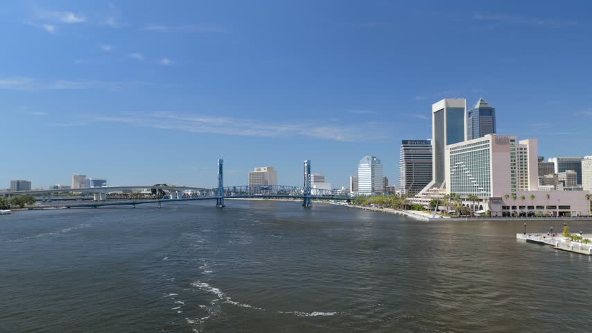 Aerial view of the Jacksonville skyline and the Main Street Bridge spanning the St. Johns River under a clear blue sky in Jacksonville, Florida, United States.