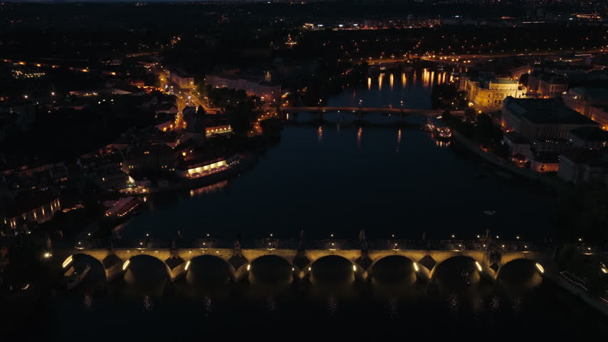 Charles Bridge Crosses The Vltava River In Prague, Czech Republic, Illuminated At Night. Aerial Shot