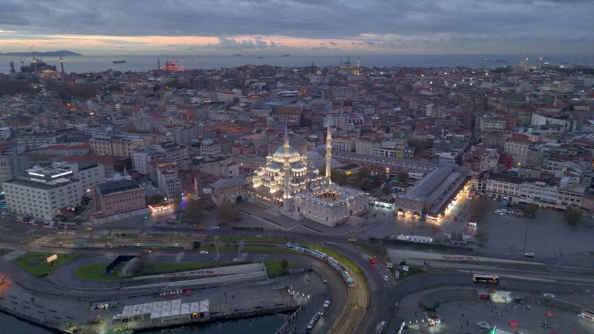 Aerial view of Istanbul at sunset, featuring the Bosphorus, a grand mosque, ferries, waterfront roads, historic buildings, and the city skyline glowing under a dramatic evening sky over Istanbul.