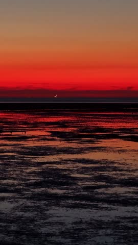Aerial view of the vibrant sunset reflecting over the tidal flats of the Wadden Sea in Eemshaven, Groningen, Netherlands.