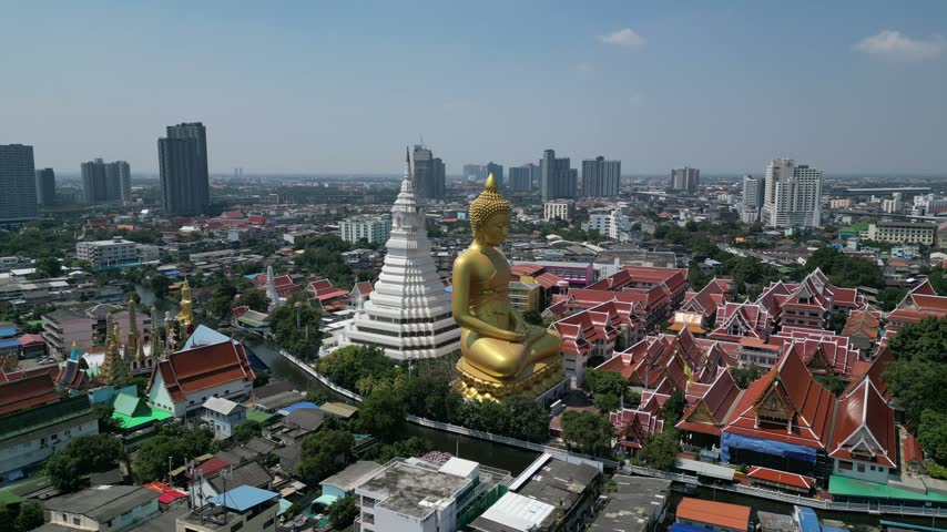 Aerial view circling the giant golden phra si ariya mettrai buddha statue and white stupa at wat paknam phasi charoen temple, a famous landmark amidst the cityscape of Bangkok, Thailand.