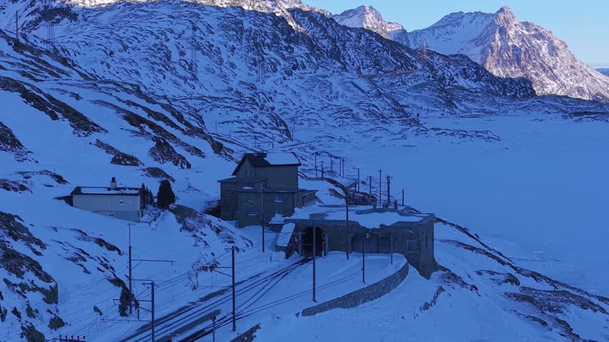 Aerial view of Ospizio Bernina surrounded by snow-covered mountains and railway tracks in Poschiavo, Graubunden, Switzerland.