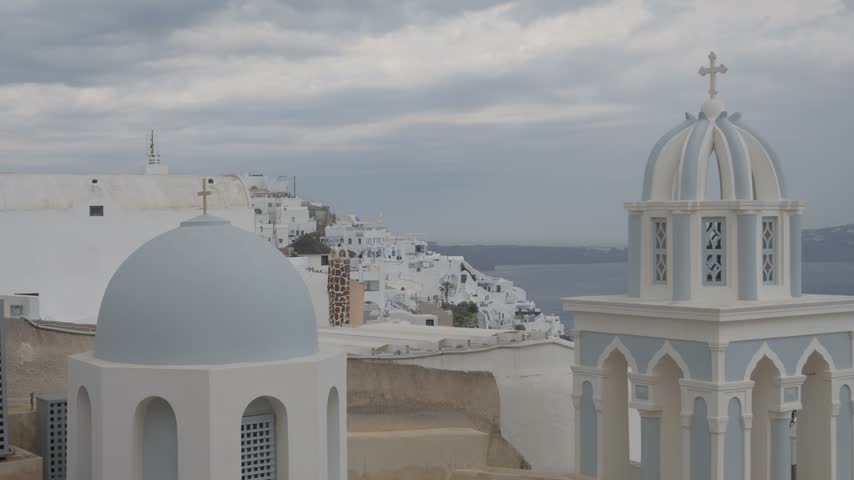 Traditional Greek Orthodox churches with iconic blue domes in Fira, Santorini, offering a serene view of the Aegean Sea.