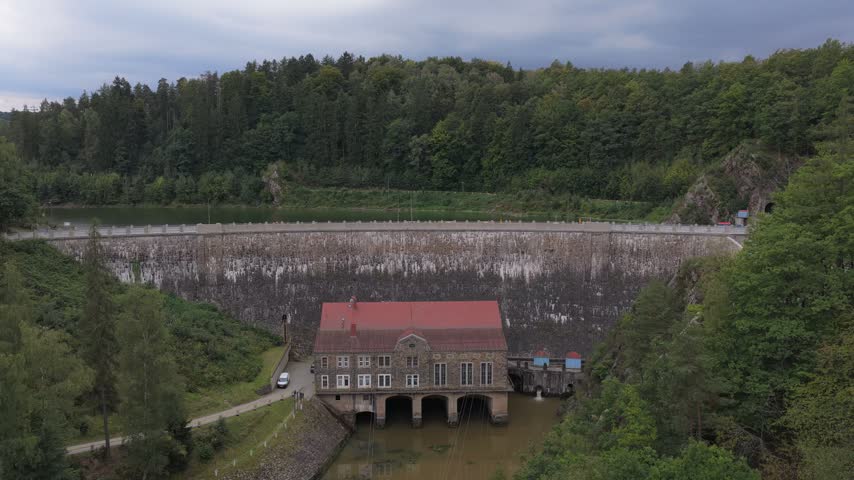 Aerial view of Zlotniki Dam with its stone wall and historic power station building surrounded by lush forest in Zlotniki Lubanskie, Lower Silesian Voivodship, Poland.