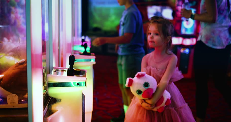 Little Girl Holding Plush Prize Toy While Exploring Colorful Neon Arcade