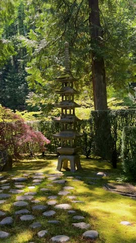 Tiered stone pagoda lantern and stepping stones in a moss garden beneath towering evergreens at a Japanese garden in Portland