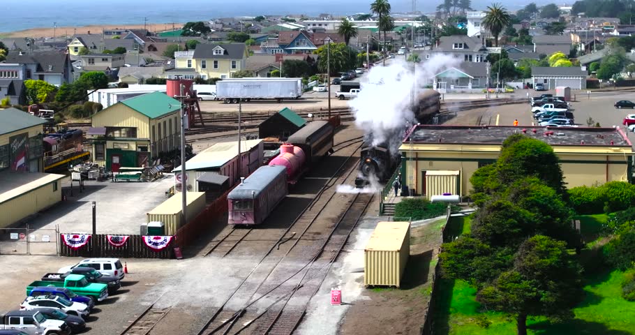 Aerial view of a historic steam train emitting smoke while arriving at the depot in Fort Bragg, California, United States.