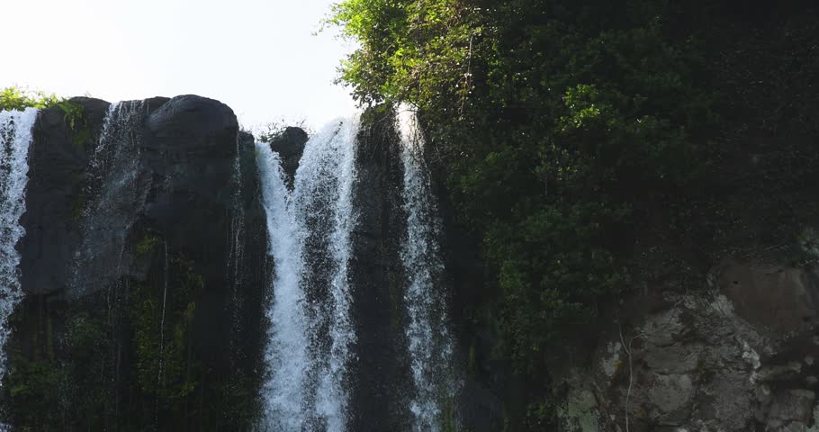 Jeongbang waterfall in Seogwipo, Jeju island, Jeju-do, South Korea, water streams falling over a dark basalt cliff into a pool by the sea on a sunny day, nature and volcanic landscape, Seogwipo-si
