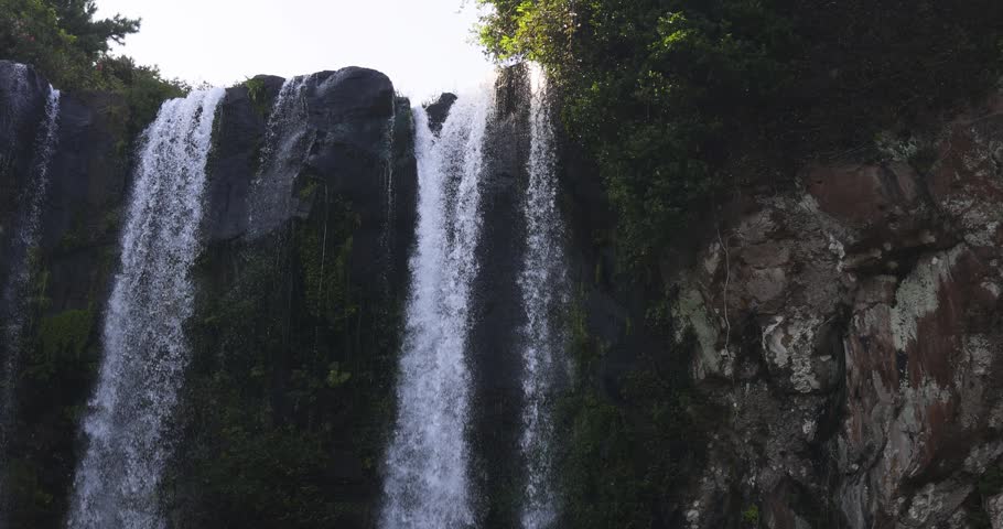 Jeongbang waterfall in Seogwipo, Jeju island, Jeju-do, South Korea, water streams falling over a dark basalt cliff into a pool by the sea on a sunny day, nature and volcanic landscape, Seogwipo-si

