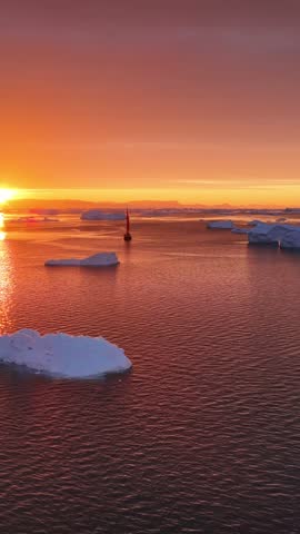 Aerial view of Ilulissat Icefjord at sunset with a small boat navigating among floating icebergs in the calm water Ilulissat, Avannaata Kommunia, Greenland.
