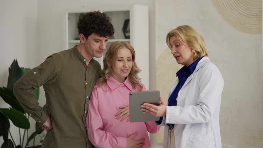 Smiling female obstetrician showing baby ultrasound image to expecting couple