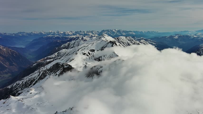 Aerial view of snow-capped peaks of the Alps rising above a dense sea of clouds in the mountains of Austria.