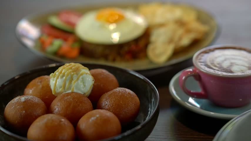 Fried dough balls loukoumades with vanilla ice cream topping and hot latte coffee on wooden table at cafe restaurant