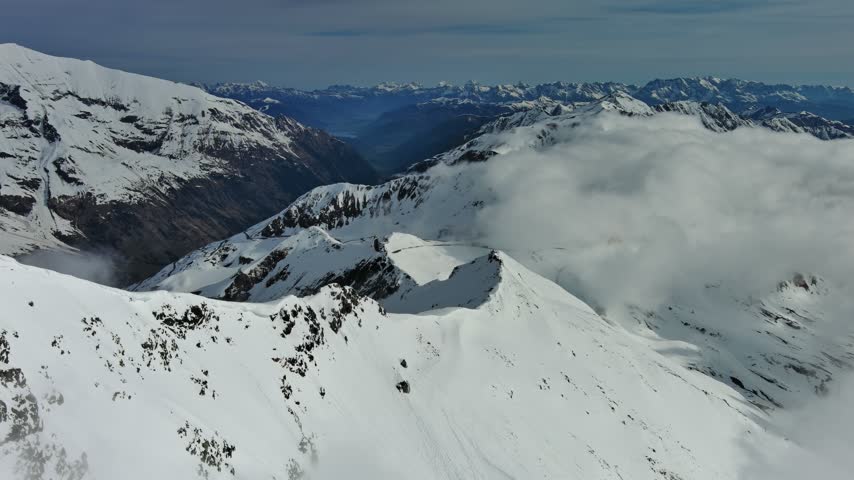 Aerial view of the snowy Alps mountain range with rugged peaks and clouds in Austria.
