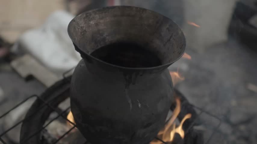 Spoon checking cooked beans from a blackened metal pot over an open fire. Rustic cooking equipment, homemade food and traditional Colombian cuisine in an improvised kitchen.