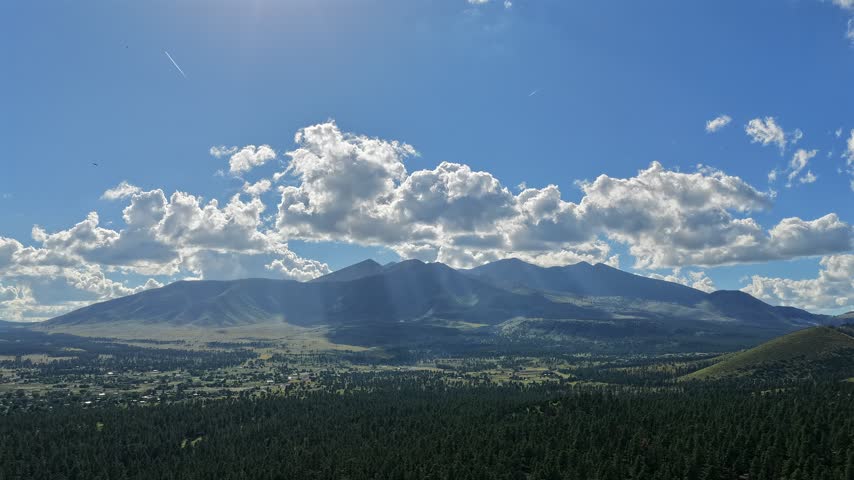 Aerial view of the San Francisco Peaks with swift moving clouds and afternoon light over the forested landscape in Flagstaff, Arizona, United States.