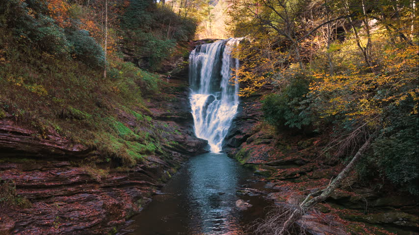 Autumn view of Dry Falls in the Nantahala National Forest, North Carolina. Waterfall with walk-behind trail framed by colorful forest and rocky boulders.