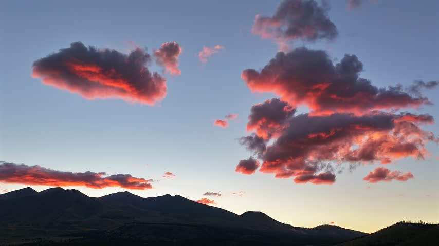 Aerial view of San Francisco Peaks with vibrant sunset clouds drifting over the mountain range in Flagstaff, Arizona, United States.