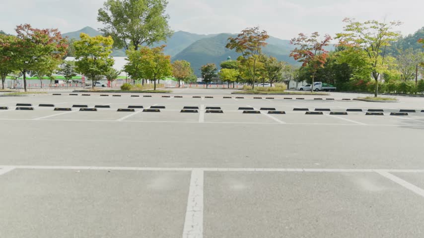 Wide view of a parking lot with horizontal parking lines, autumn trees, and a mountain landscape in the background.