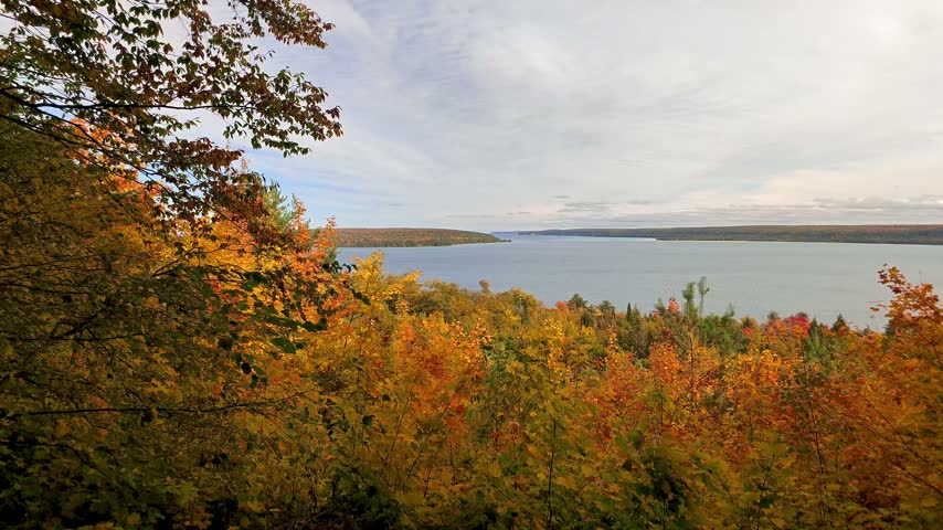 Colorful autumn forest with vibrant trees overlooking a vast lake Superior under a cloudy sky in the upper peninsula of Michigan.